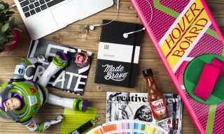 A table, with a MadeBrave branded Moleskine, HoverBoard, and various other items