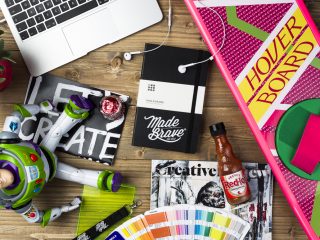 A table, with a MadeBrave branded Moleskine, HoverBoard, and various other items