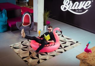 Employer Brand Culture A man sitting within an inflatable pink flamingo pool-toy, with a cocktail and reading a book