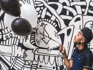 12 Practical Ideas for Creative Freelancers Looking to Get Paid Work man holding a balloon in front of a wall covered in black and white illustrations