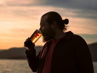 Man drinking a pint of Tennent's lager on a beach with sunset in the background