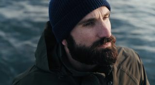 Photo of man with a beard wearing a hat next to the water