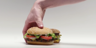 Burger King Ad A hand about to pick up a burger king whopper to reveals a mcdonalds hamburger behind it