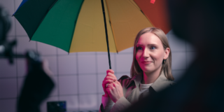 Behind the Scenes - Emma with Cocktail Umbrella woman in a trench coat holding a rainbow coloured umbrella