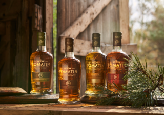 four bottles of Tomatin whisky sitting in front of a wood floor with pine branch in front of them