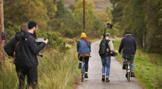 man shoots with steadicam with actors on bikes