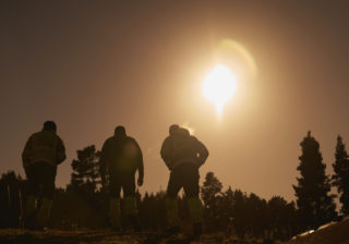Three men walking through a field, silhouetted against the rising sun