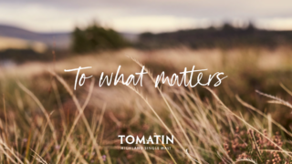 Blurred photo of fields at tomatin with white hand-written text overlayed 'to what matters' and tomatin logo in white below