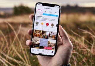 photo of hand holding an iphone which has tomatin instagram feed showing on it