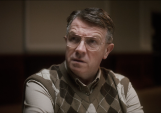 closeup photo of character, Neil, who is an older man with glasses and a plaid sweater vest