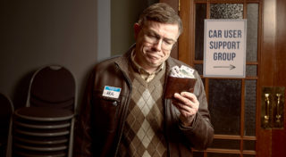 closeup photo of character, Neil, who is an older man with glasses and a plaid sweater vest