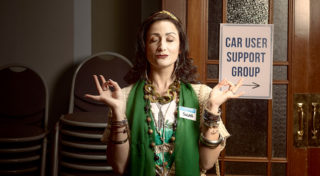 closeup photo of character, Susan, who is a middle aged woman with a lot of jewellery and a green top