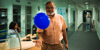 Blue Balloon Campaign - Global man in a button up shirt in an office keeping a blue balloon in the air