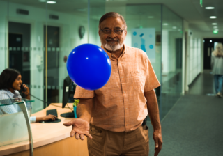 Blue Balloon Campaign - Global man in a button up shirt in an office keeping a blue balloon in the air