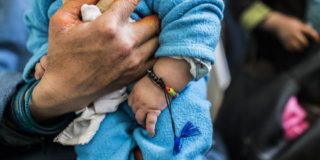 Immunity Charm photo of someone holding a baby who is wearing an immunity charm with multi-color beads