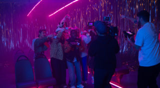 BTS shot of cameraman filming and Director giving direction to cast.