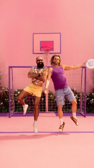 a photo of two athletic men jumping up in the air with a frisbee with a pink background