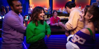photo of a smiling woman in a green top accompanied by her friends, all standing at the bar