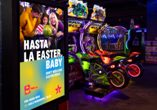 A bright digital poster on a pillar within the arcade section of the bowling centre. It showcases a family having fun bowling and is to encourage uptake of their easter deals.