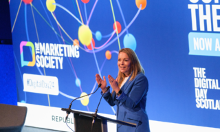 The Marketing Society Digital Day 2024 photo of a woman on stage hosting the marketing society digital day 2024 with blue screen and colorful graphics in the background