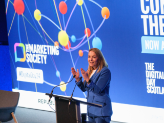 The Marketing Society Digital Day 2024 photo of a woman on stage hosting the marketing society digital day 2024 with blue screen and colorful graphics in the background