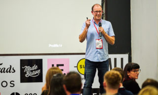 Jamie Axford - Prolific North LIVE photo of jamie axford, creative director at madebrave, standing on a conference stage with an audience watching