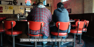 still frame of two men sitting on stools talking in a diner