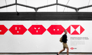 a photo of a man walking in front of a white and red HSBC billboard