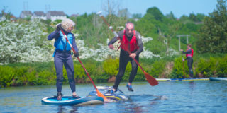 two older people paddleboarding. One is about fall into the water