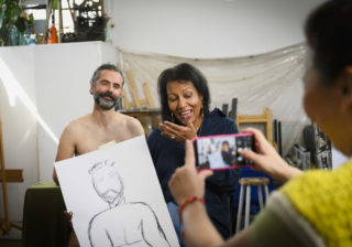 man holding up a lifedrawing sketch of himself while people take photos