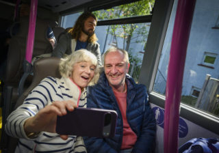 Two older people taking a selfie on a bus