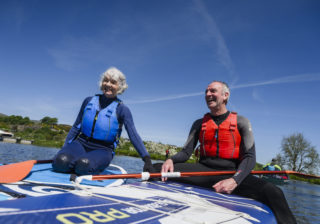 two older people paddleboarding and sitting on their paddleboards