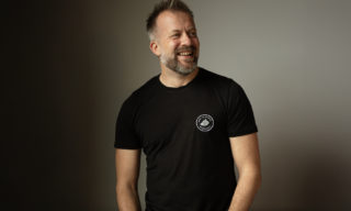 Andrew Dobbie | Founder / CEO, MadeBrave a photo of andrew dobbie, ceo of madebrave wearing a black shirt and standing in front of a cream wall