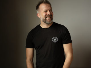 Andrew Dobbie | Founder / CEO, MadeBrave a photo of andrew dobbie, ceo of madebrave wearing a black shirt and standing in front of a cream wall