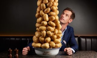 a photo of andy murray looking up at a towering stack of potatoes