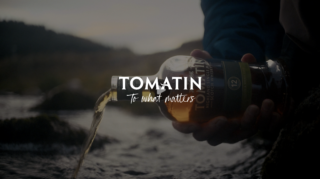 photo of a bottle of whisky being poured into a river with 'tomatin' written over the top in white text