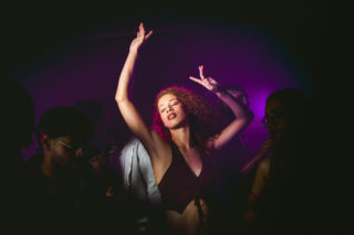 Photo of a woman dancing on a dance floor with pink and purple light washing over