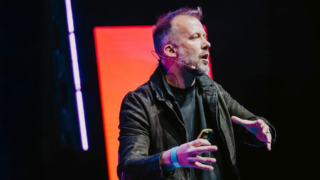 a photo of andrew dobbie up on stage with neon lights behind him