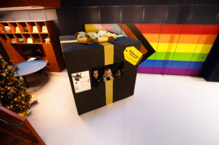 photo of three people inside of a giant present wrapped in black paper with a golden bow