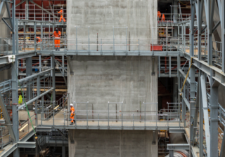Coriant Brand photo of a several people in orange jumpsuits on scaffolding surrounding a concrete pillar