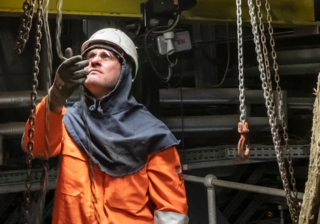 Coriant Brand photo of a man in a hardhat and orange jumpsuit inspecting a chain