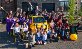 Kids Make Glasgow - Group Shot photo of man in a small yellow car with 20 kids and other adults smiling with hands in the air
