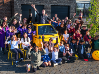 Kids Make Glasgow - Group Shot photo of man in a small yellow car with 20 kids and other adults smiling with hands in the air